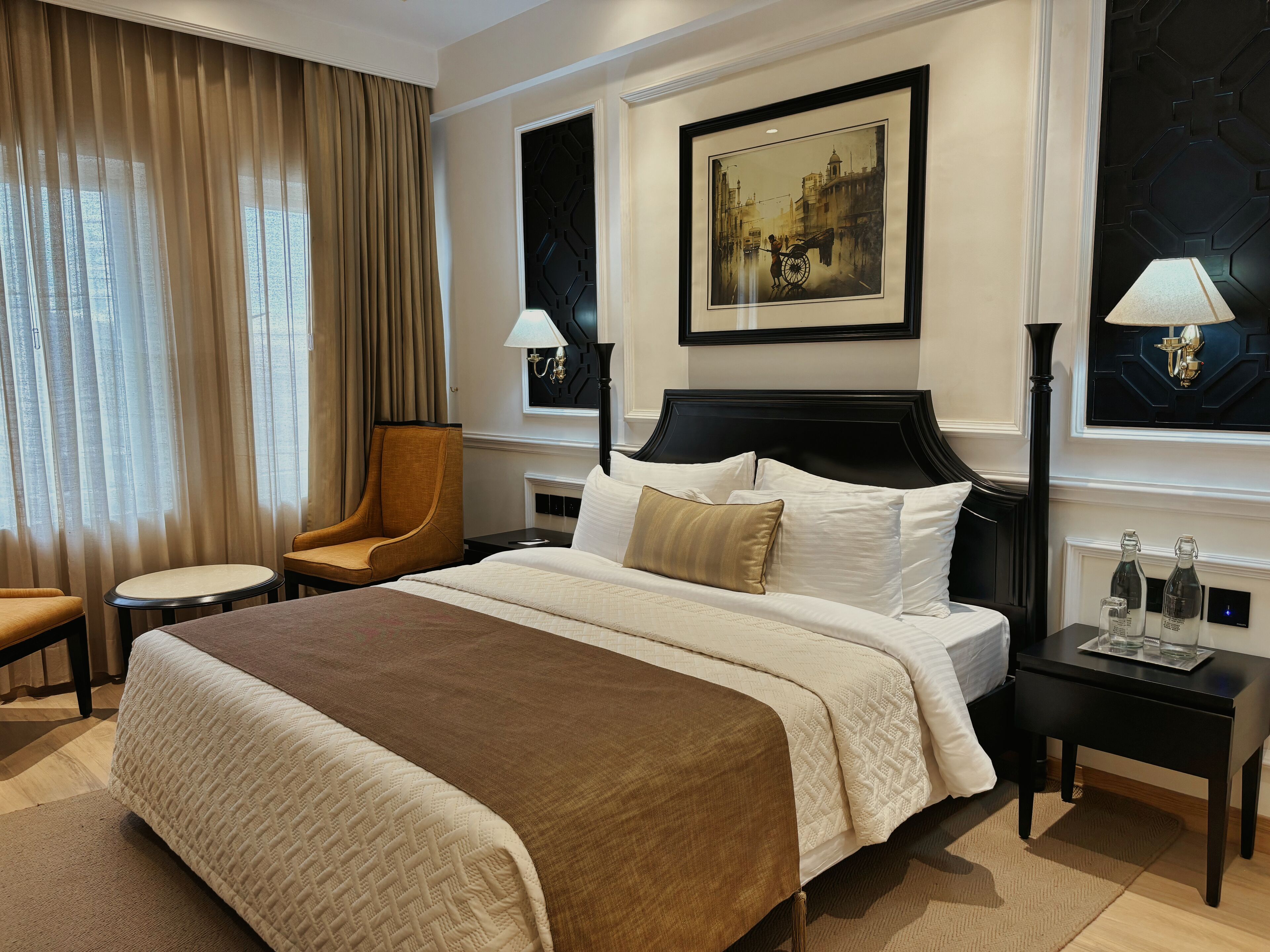 Una habitación de hotel con una cama grande, una silla, una mesita de noche y un cuadro en la pared.
