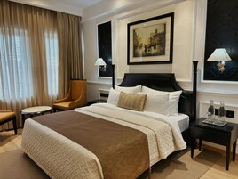 A hotel room with a large bed, a chair, a nightstand, and a painting on the wall.