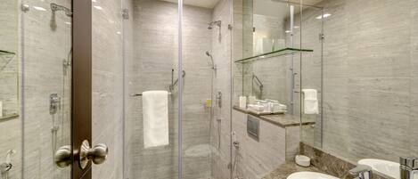 Casa de banho moderna com chuveiro separado por vidro, sanita e duas lavatórios com tampos em mármore.