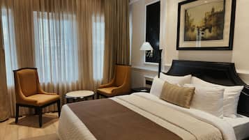Una habitación de hotel con una cama grande, dos sillones, una mesita redonda y un cuadro en la pared.