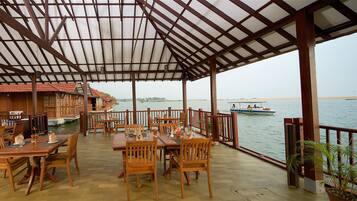 A restaurant with wooden tables and chairs, a covered patio, and a view of the water.