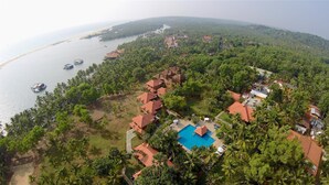 Vista aérea de um resort com vários edifícios, piscina e barcos na água.