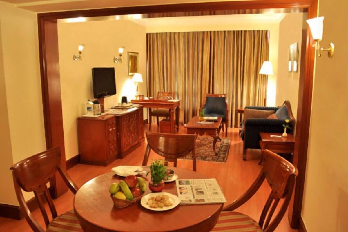 Een hotelkamer met een eethoek, een bank, een televisie en een gordijn.