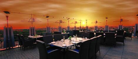 An outdoor dining area with tables and chairs, set against a sunset backdrop.