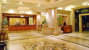 Un vestíbulo de hotel con mostrador de recepción, una araña, columnas y un suelo con diseño.
