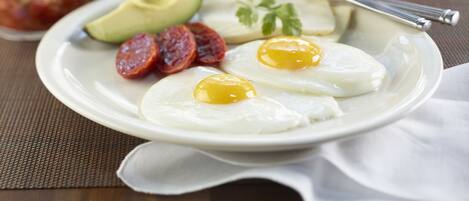 A breakfast plate with eggs, avocado, and chorizo, a coffee mug, and a glass of orange juice on a table.