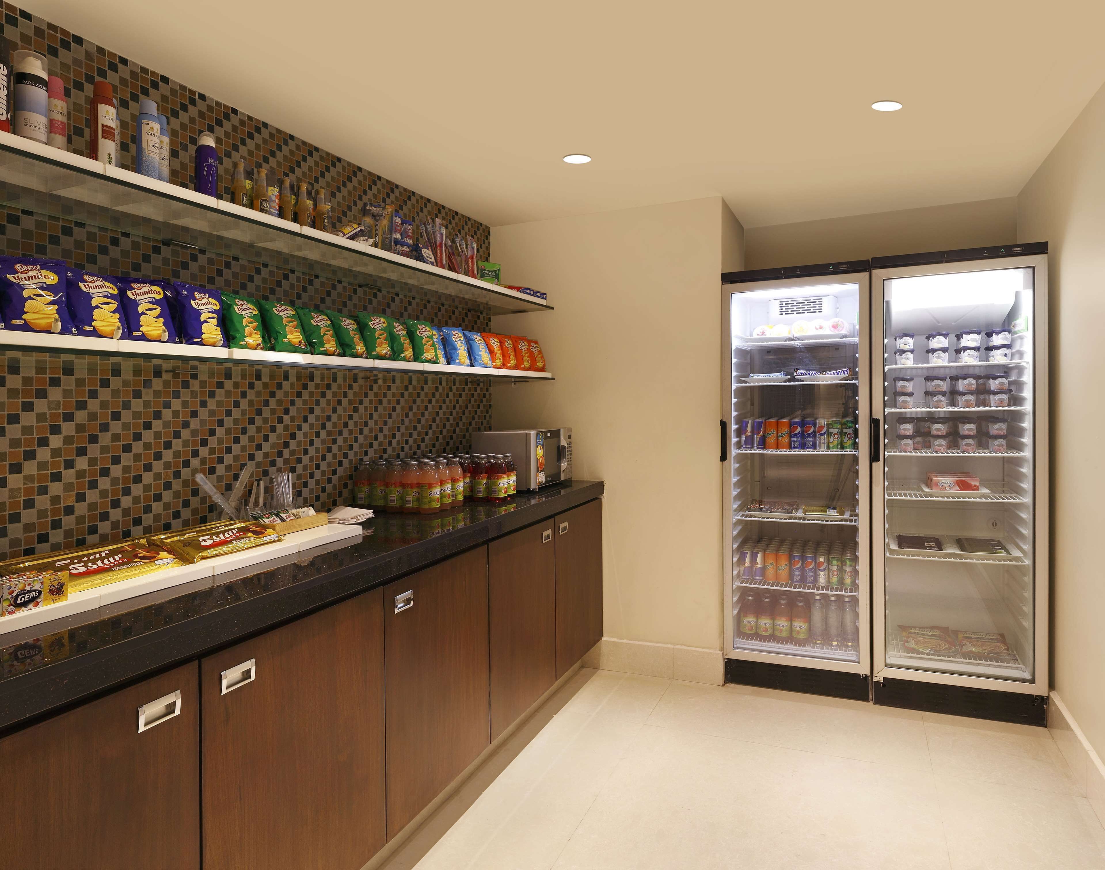 Una kitchenette con estantes llenos de aperitivos, salsas y bebidas, y un refrigerador con varias opciones.