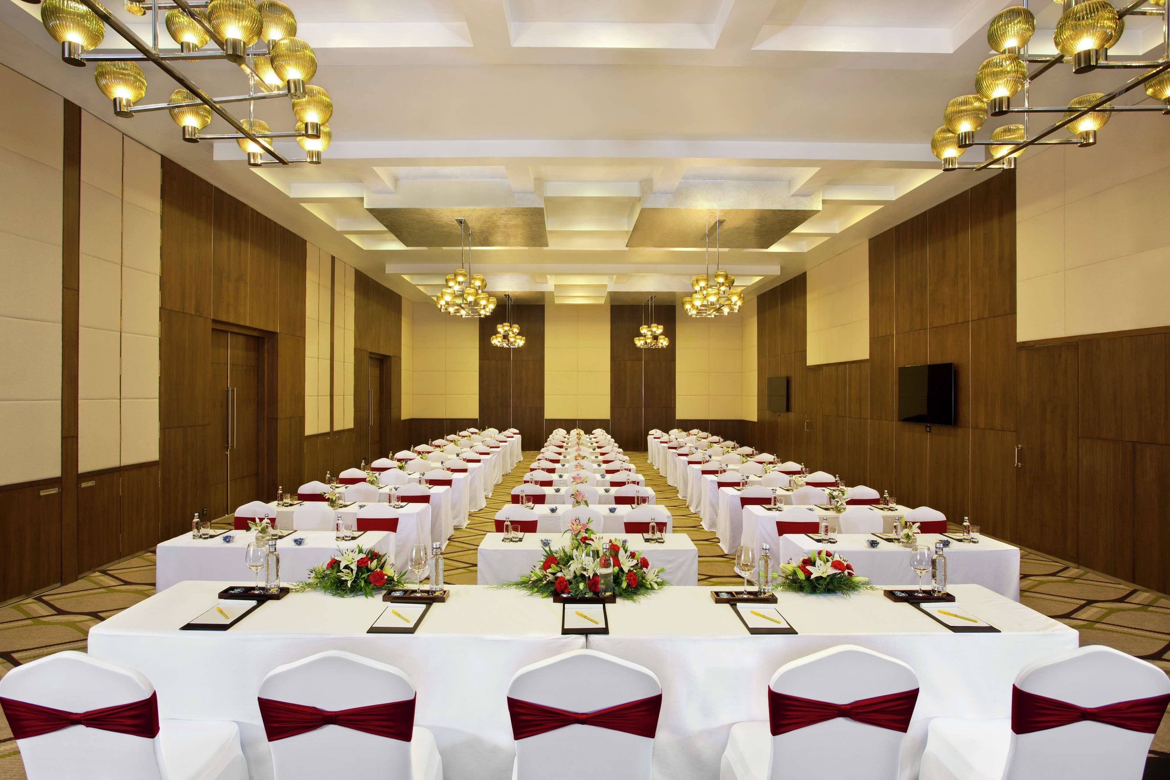 A conference room with rows of white tables, red sashes, and chandeliers.
