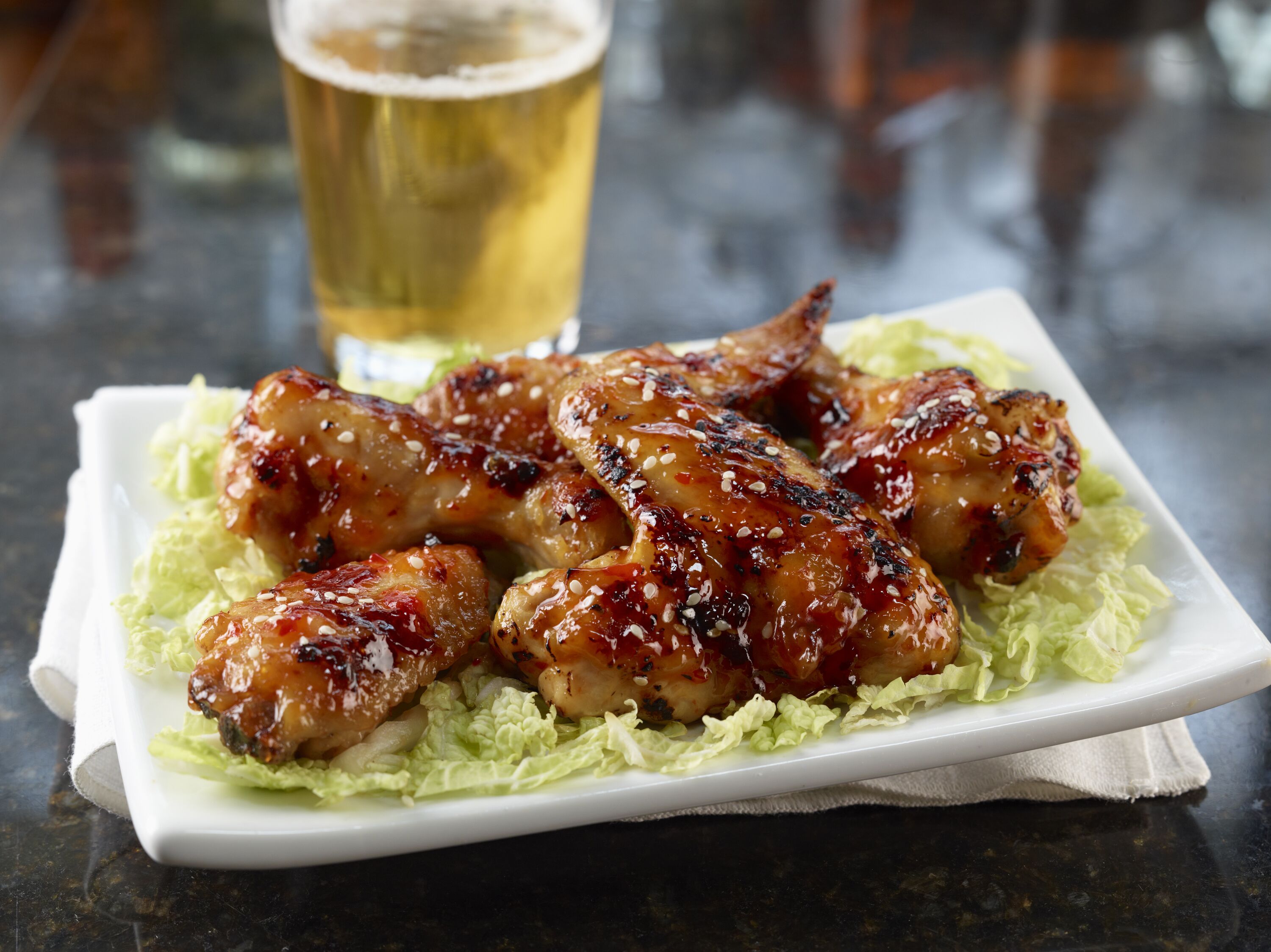 Ein Teller glasierte Chicken Wings auf einem Salatbett, dazu ein Glas Bier.
