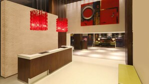 Una moderna zona de recepción con un mostrador de madera, una obra de arte abstracta roja y un área de bar al fondo.