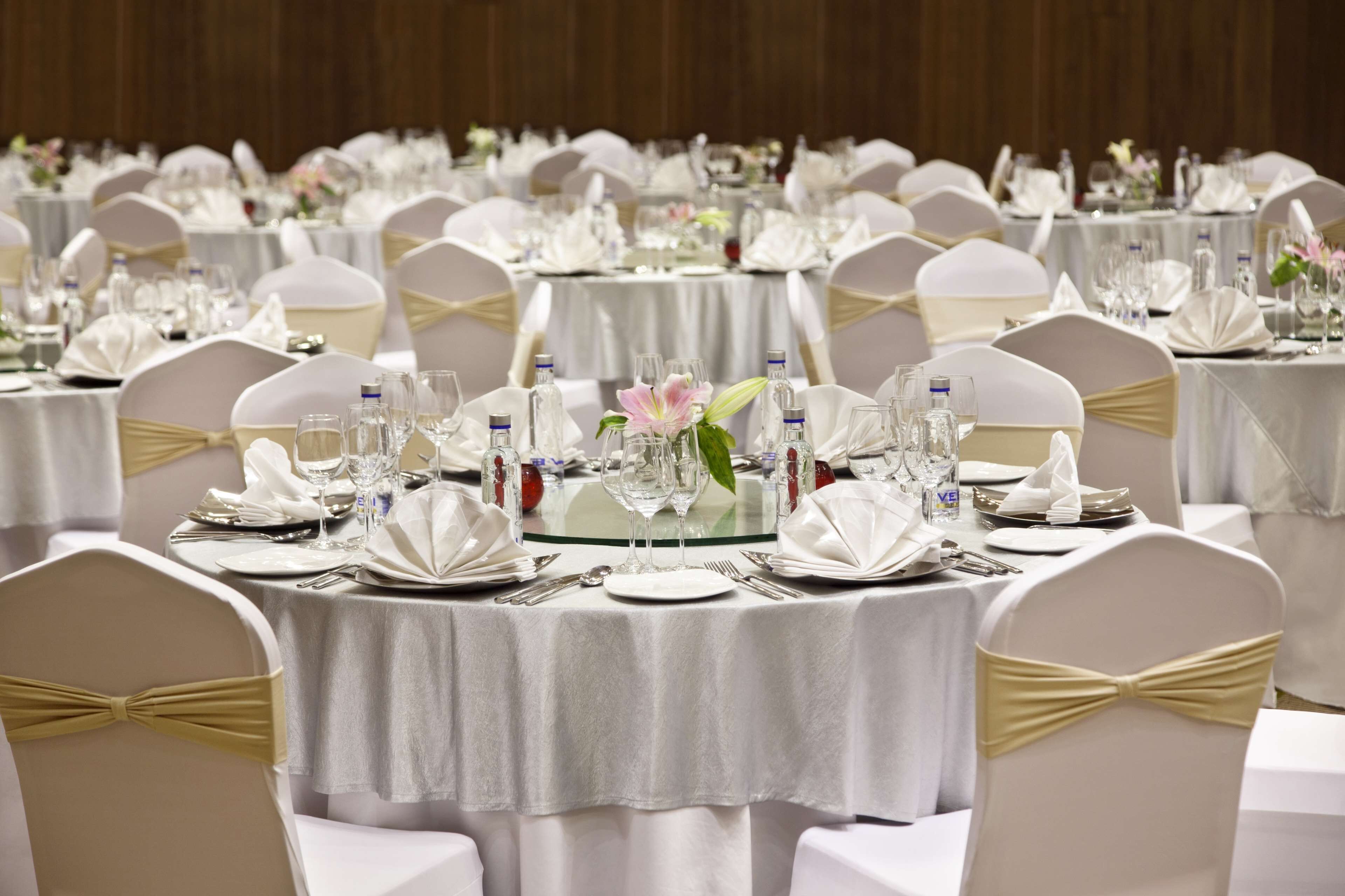 A banquet hall with round tables set with white tablecloths, gold sashes, and glassware.