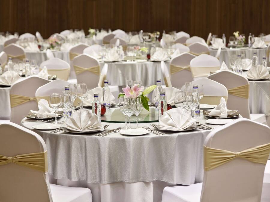 A banquet hall with round tables set with white tablecloths, gold sashes, and glassware.