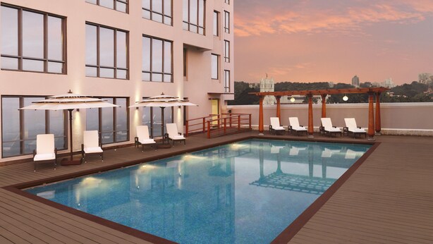 Una piscina en la azotea con sillones y sombrillas, rodeada por un edificio con ventanales amplios.