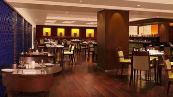 A restaurant with round tables and chairs, a bar area, and a patterned wall.