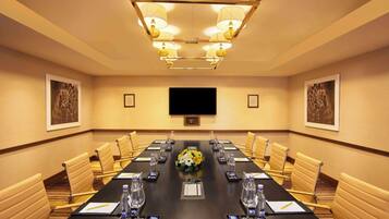 A conference room with a long table, chairs, a television screen, and a floral centerpiece.