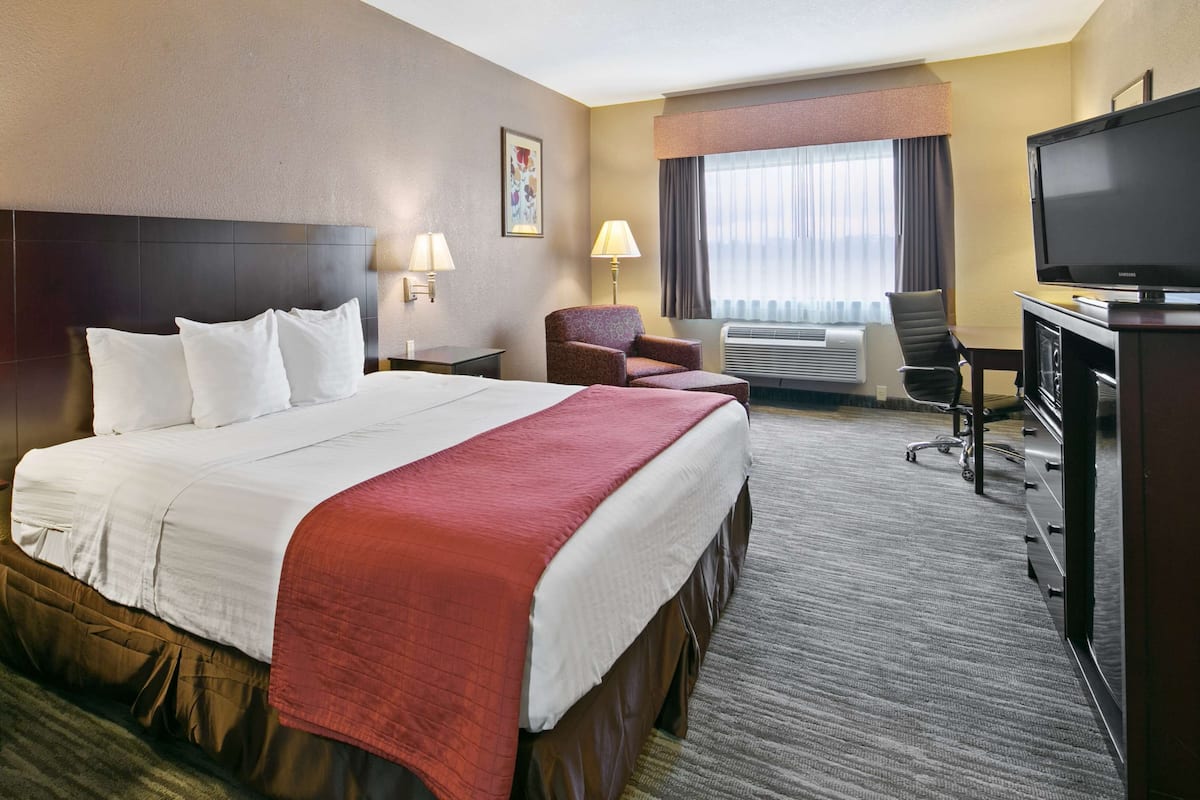 A hotel room with a large bed, two bedside lamps, a desk with a TV, a chair, and a window with curtains.