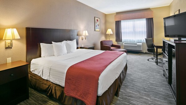 A hotel room with a large bed, two bedside lamps, a desk with a TV, a chair, and a window with curtains.