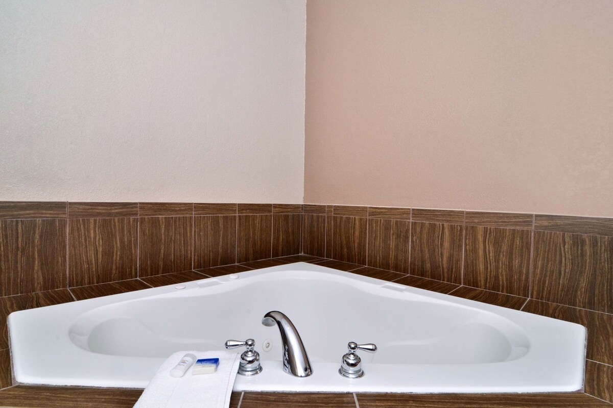 A corner bathtub with a white sink, two faucets, and a soap dispenser.