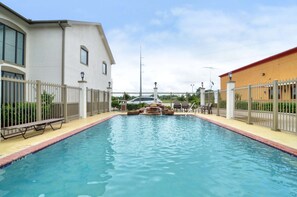 A swimming pool with a fountain, surrounded by a fence, and adjacent to buildings.