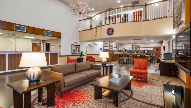 Um saguão de hotel com balcão de recepção, área de estar e escadaria para um andar superior.