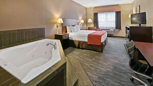 Quarto de hotel com uma banheira grande, uma cama com cobertor vermelho, uma escrivaninha com televisão e uma janela com cortinas.