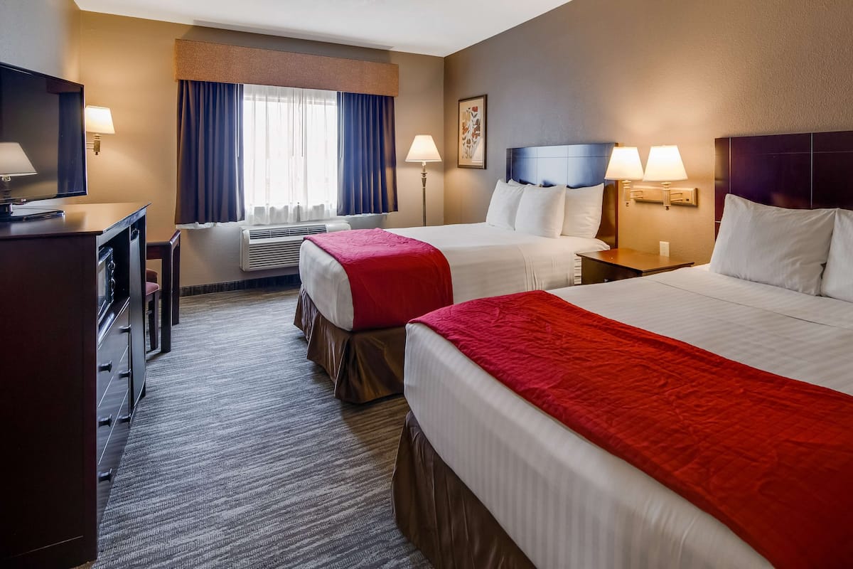 A hotel room with two beds, a desk, a chair, a TV, and a window with curtains.