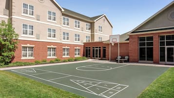 A courtyard with a basketball court, a tennis court, and a building with multiple windows and a door.