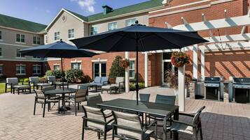 An outdoor patio area with tables and chairs, umbrellas, and barbecue grills.