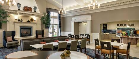 A spacious hotel lobby with a fireplace, seating areas, and a kitchen visible in the background.