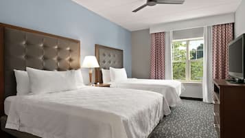 A hotel room with two beds, a ceiling fan, a TV, and a window with curtains.