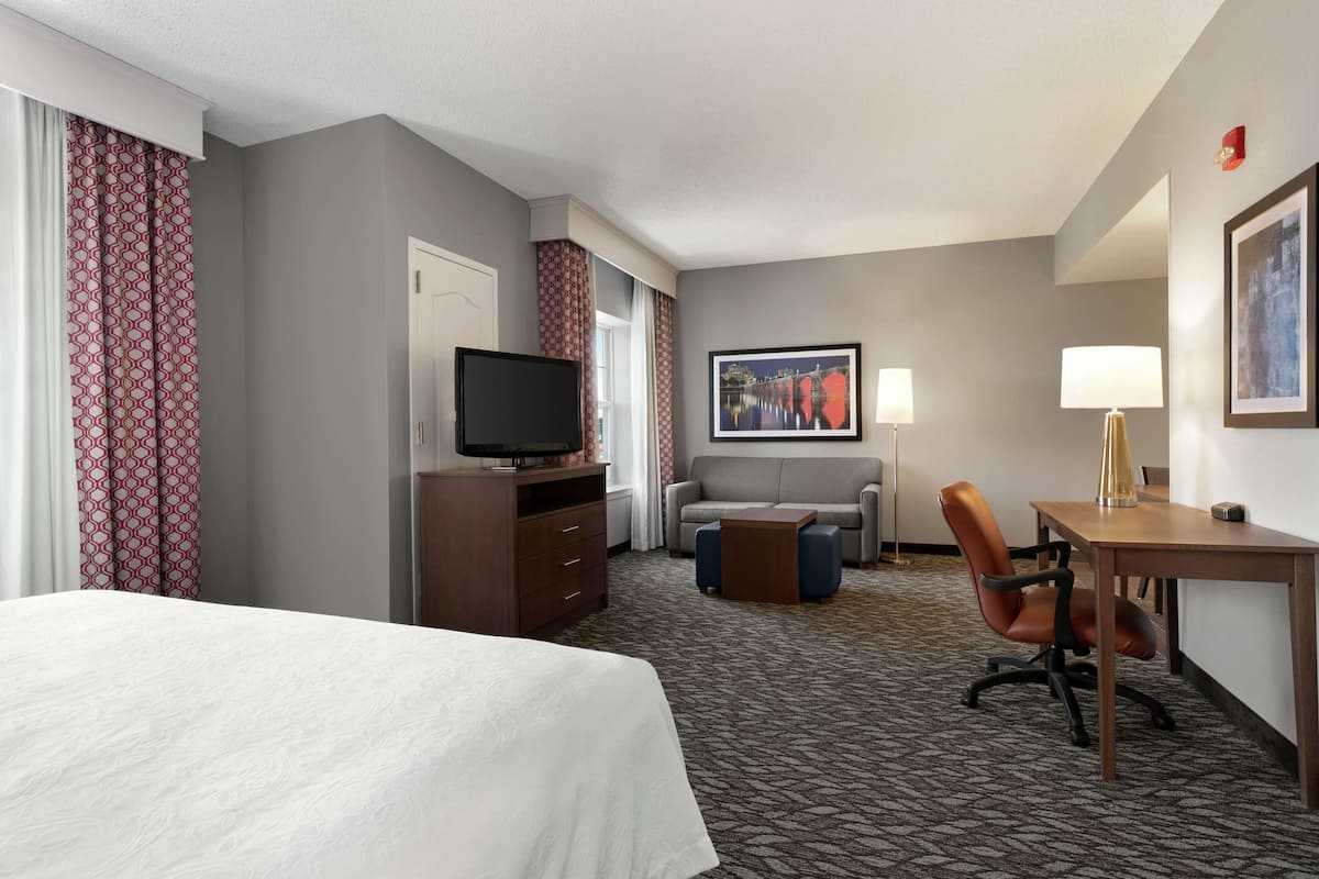 A hotel room with a bed, a desk, a chair, a television, a sofa, and a painting on the wall.