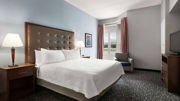 A hotel room with a large bed, a desk with a lamp, a chair, a television, and a window with curtains.