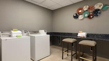 Une chambre d’hôtel équipée d’une kitchenette, de deux tabourets de bar et d’un égouttoir à vaisselle fixé au mur, contenant différentes assiettes.