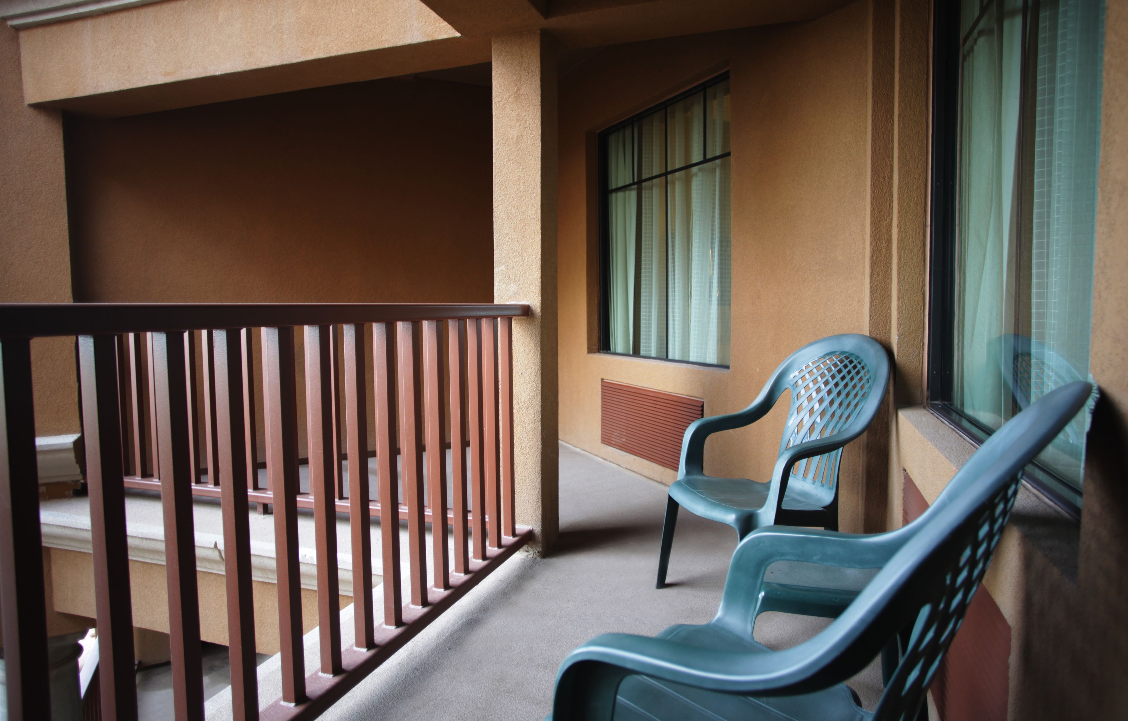 A balcony with a metal railing, two plastic chairs, and a window with blinds.