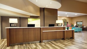 A reception area with a wooden reception desk, two lamps, a green sign, and a seating area with a blue sofa and a plant.
