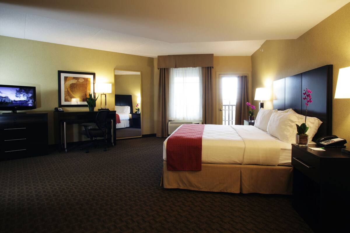 A hotel room with a bed, desk, chair, television, and a view of the outside balcony.