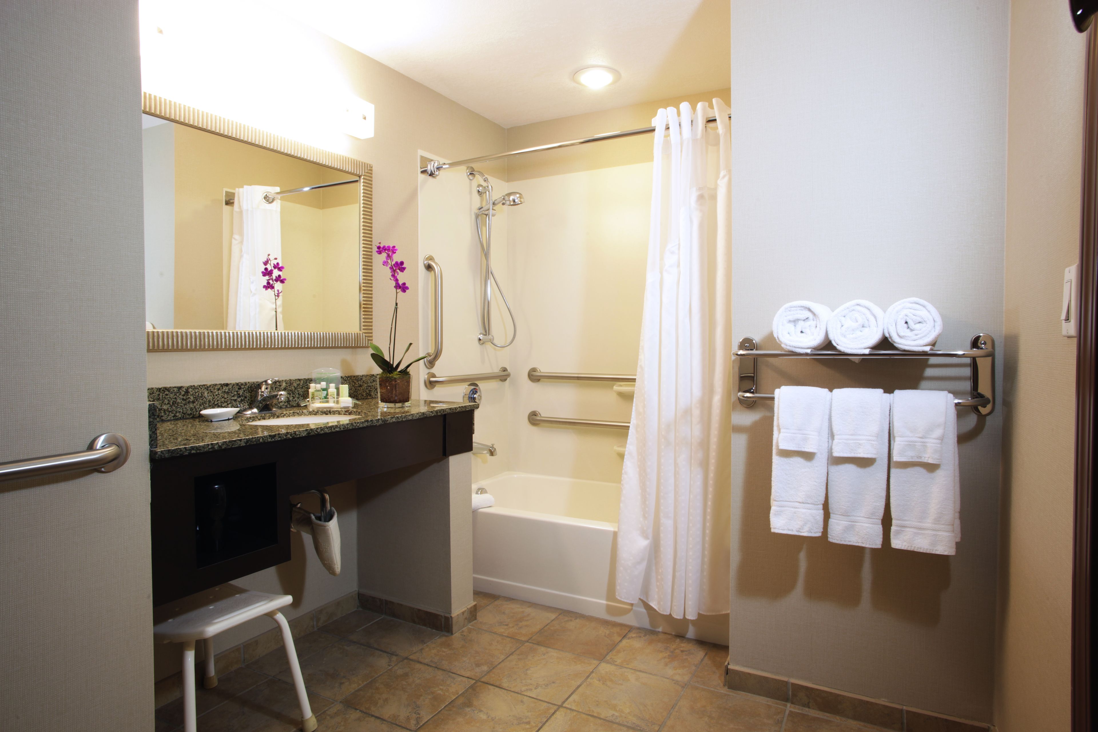 A bathroom with a shower, a bathtub, a vanity with a mirror, and a towel rack with towels.