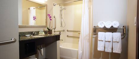 A bathroom with a shower, a bathtub, a vanity with a mirror, and a towel rack with towels.