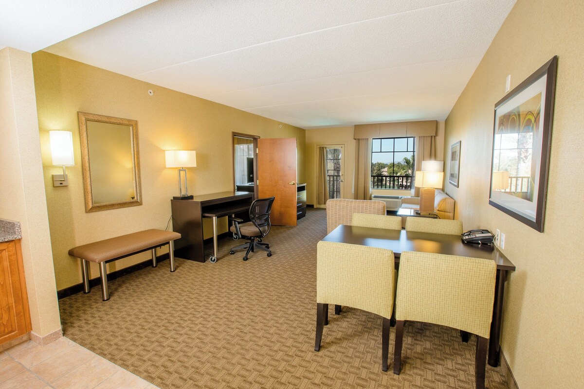 A hotel room with a desk, chair, dining table, and a view of the outdoors.