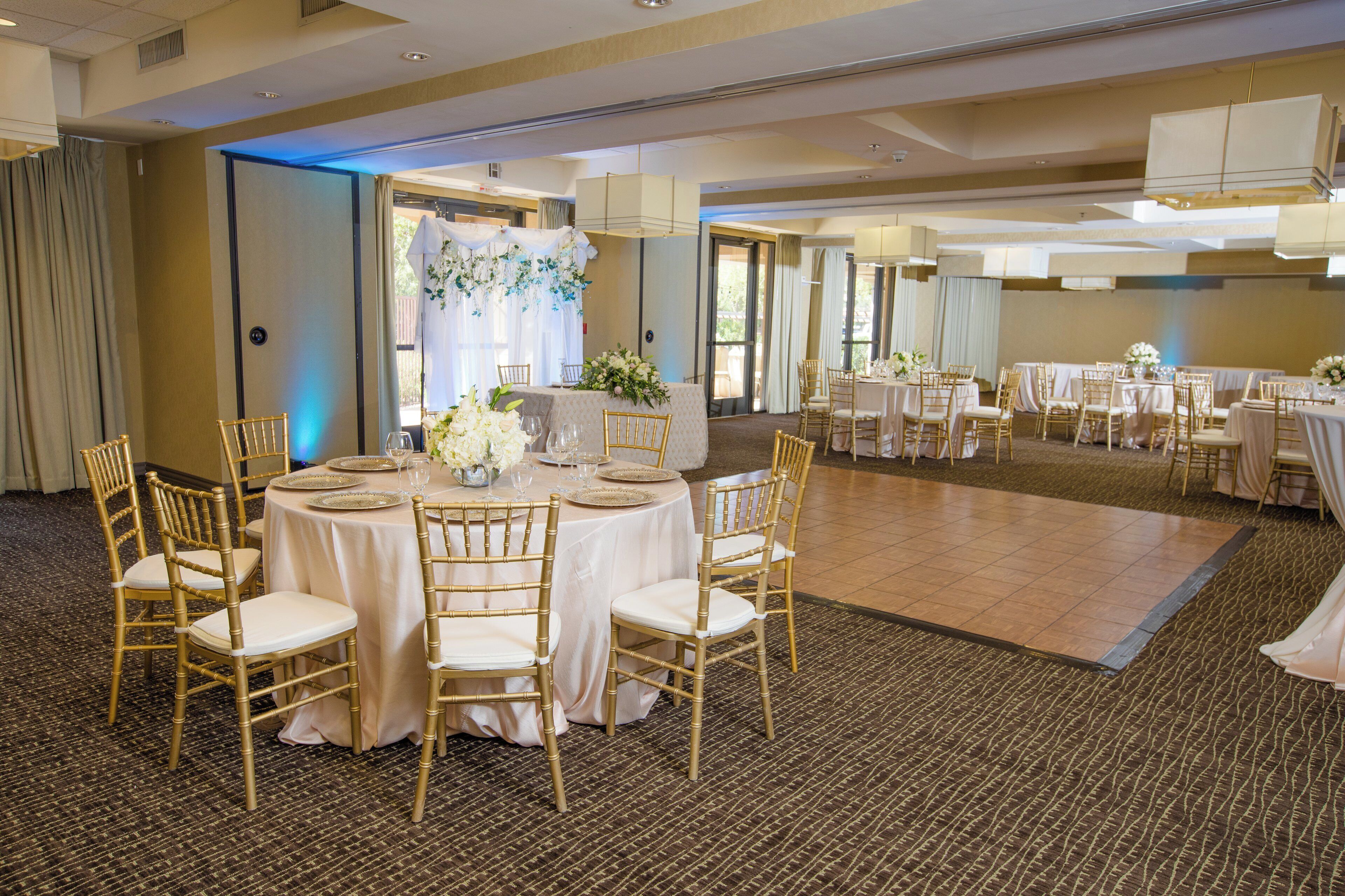 A banquet hall with round tables, gold chairs, and a floral centerpiece.
