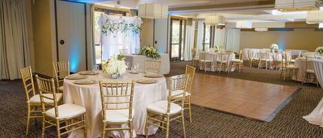 A banquet hall with round tables, gold chairs, and a floral centerpiece.