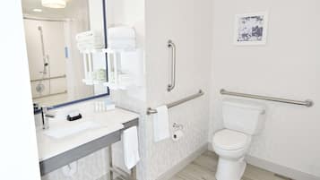 A modern bathroom with a sink, mirror, toilet, and handrails.