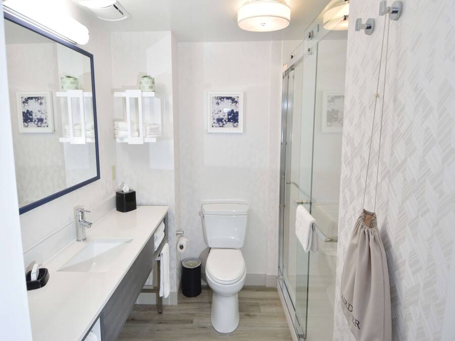 Un baño moderno con un espejo grande, lavamanos blanco, inodoro y cabina de ducha con mampara de vidrio.