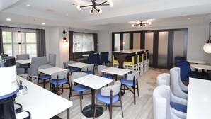 A modern dining area with multiple tables and chairs, a coffee machine, and a ceiling light fixture. - Hampton Inn Auburn (Auburn)