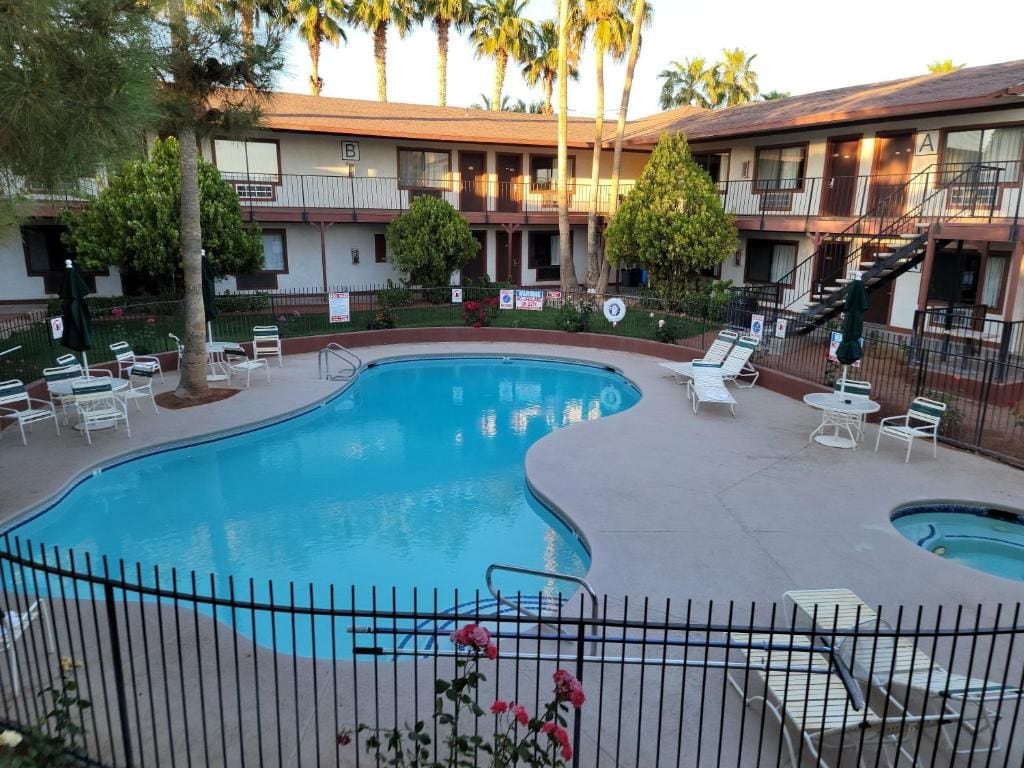 A swimming pool with lounge chairs and a fenced area, surrounded by a building with multiple balconies.