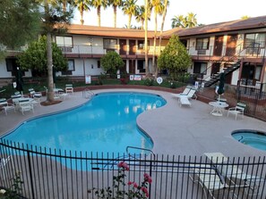 Una piscina con sillones de descanso y un área cercada, rodeada por un edificio con varios balcones.
