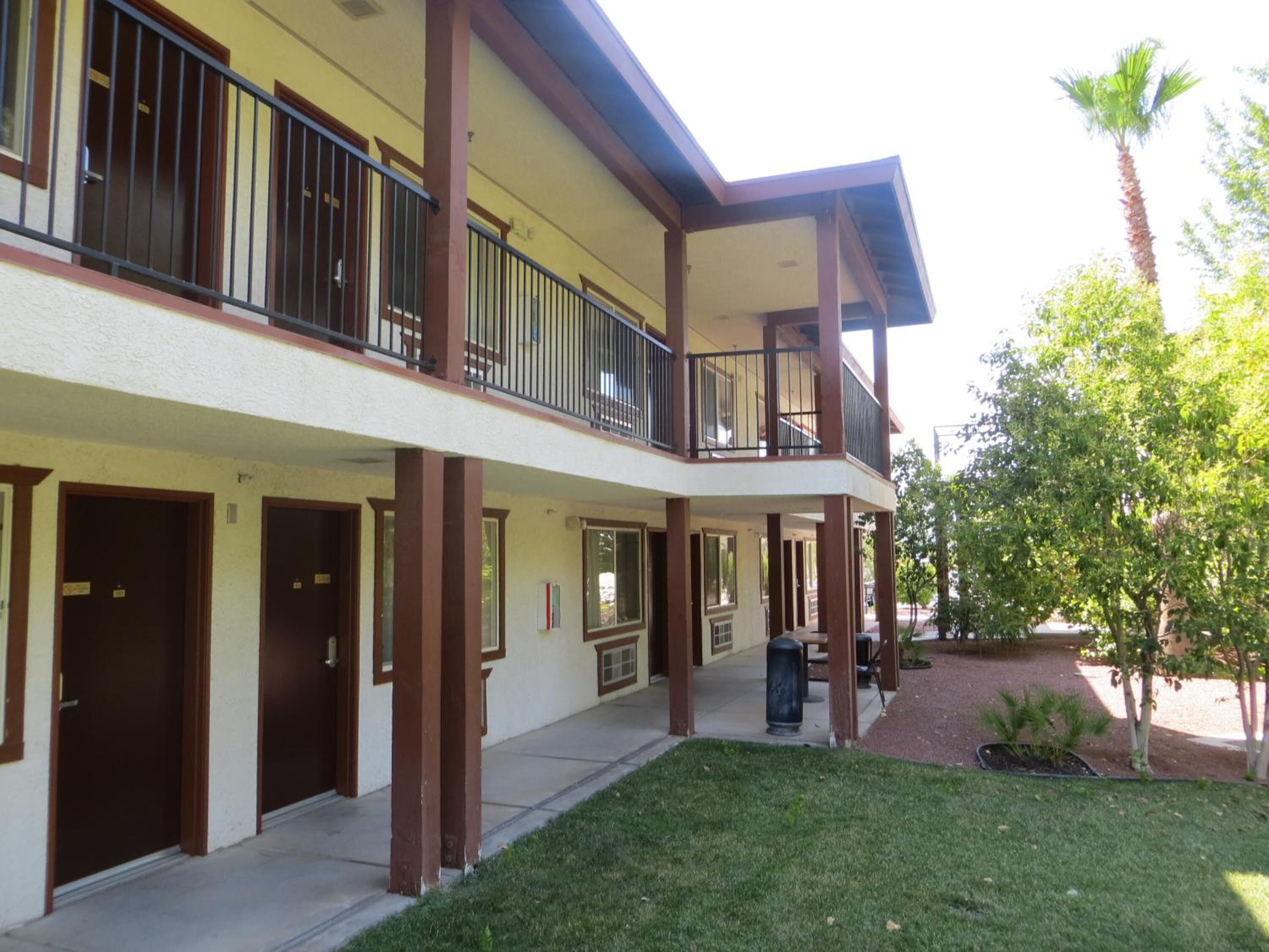 A two-story building with a flat roof, multiple balconies, and a small courtyard with grass and trees.