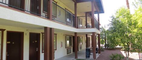 A two-story building with a flat roof, multiple balconies, and a small courtyard with grass and trees.