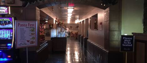 An entrance to a restaurant with a neon sign, a pasta menu, and a 'Please Wait To Be Seated' sign.