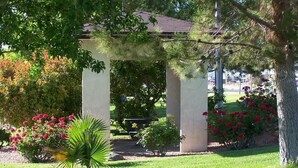 A gazebo with a tiled roof, surrounded by a well-maintained garden with various plants and flowers.